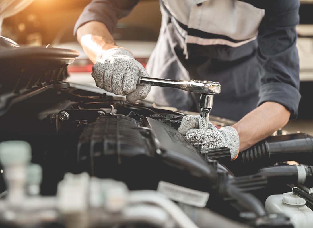 Auto Services and Fleet Insurance Programs - Auto Mechanic Working with His Hands and Servicing a Car and Repairing the Engine in the Automotive Workshop with a Wrench