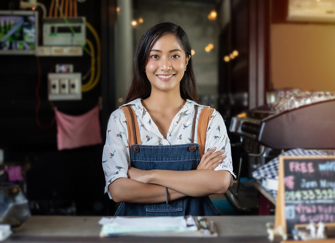 Business Insurance - Portrait of a Young Smiling Female Business Owner Standing Behind the Front Counter of Her Store with Her Arms Folded