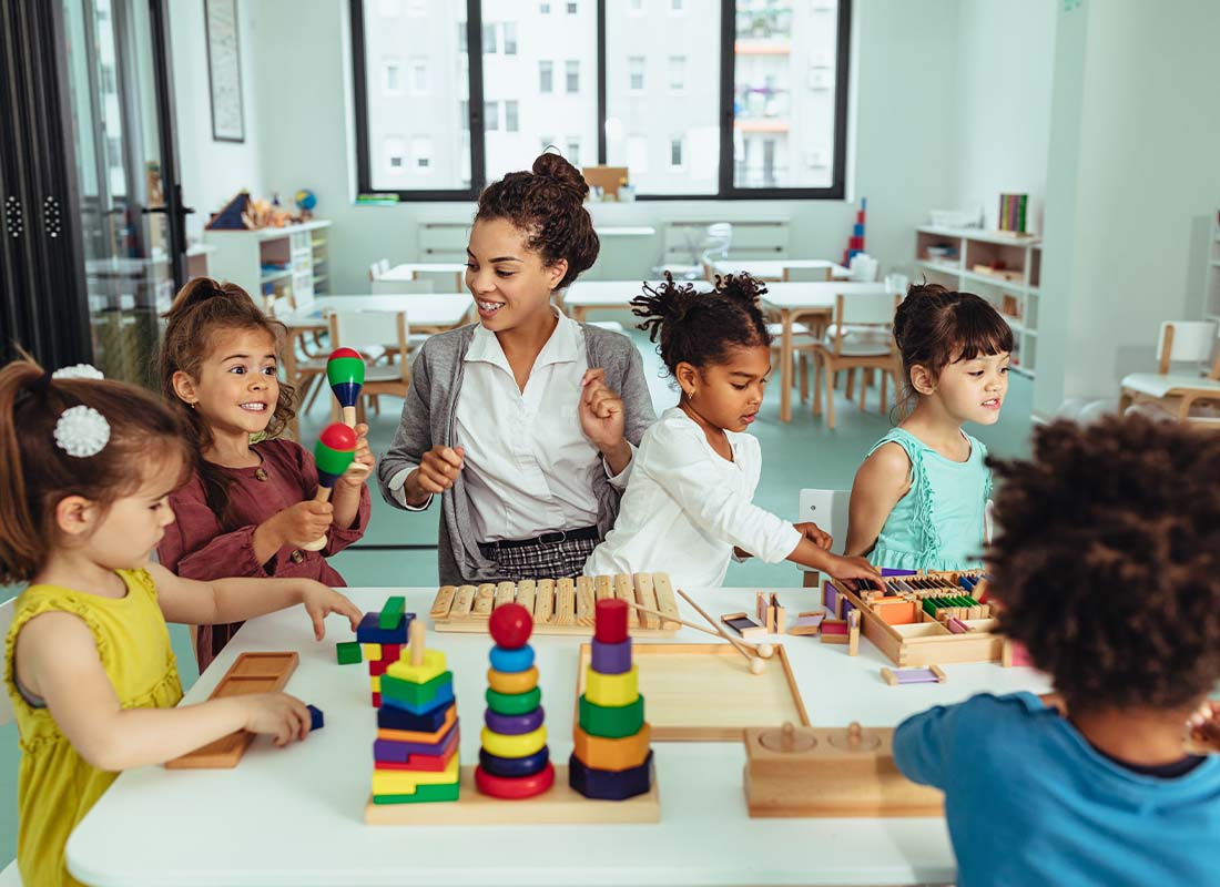 Child Care Complete Program - Day Care Employee or Kindergarten Teacher Playing with Young Children in the Classroom and Creating Artwork and Building Blocks Together
