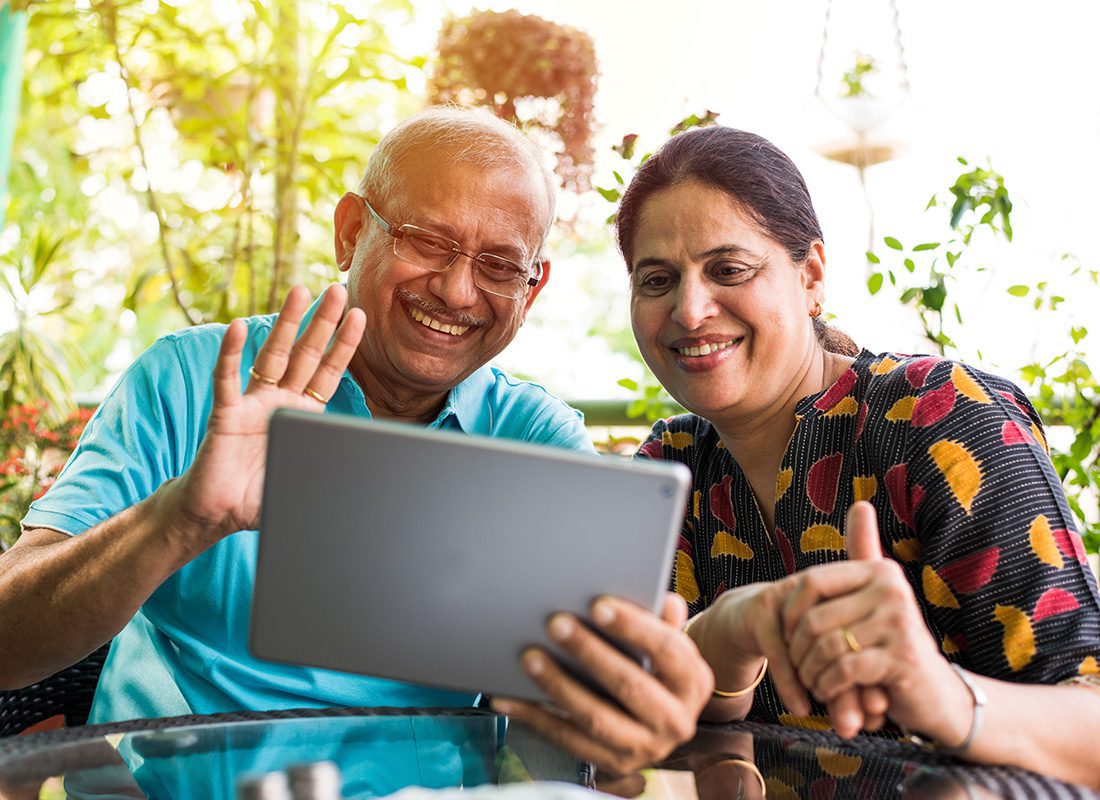 Contact - Closeup Portrait of a Mature Couple Sitting in Their Backyard Patio Surrounded by Green Plants Using a Tablet to Video Chat