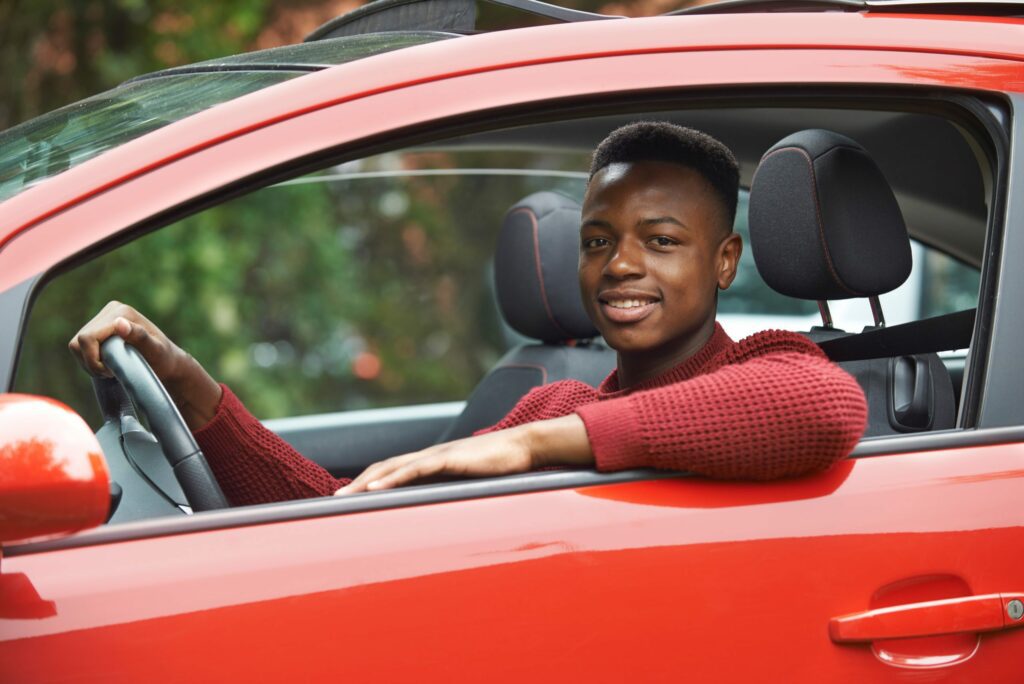 Teen sitting on the driver's side of a red car