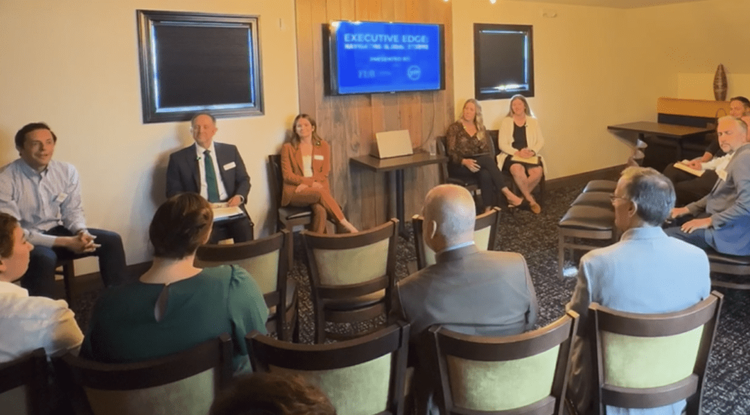 A panel of business and legal professionals seated in a semi-circle at Notch in Allentown, participating in a YMI-hosted event titled "Executive Edge: National Tariffs & Global Shifts." Audience members face the panelists in a small, warmly lit room, with a screen displaying the event title in the background.
