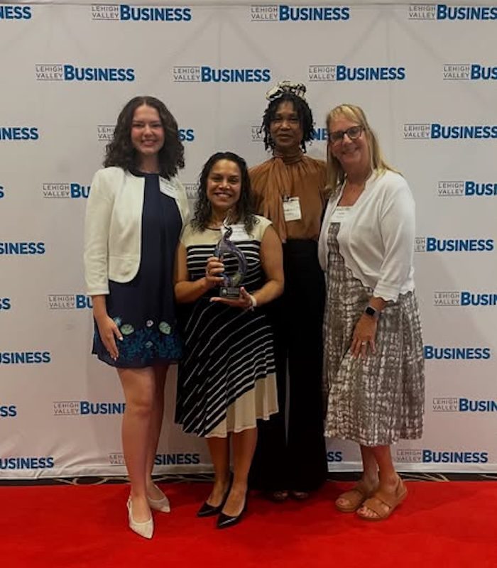 Four YMI team members standing together on the red carpet at the 2025 Empowering Women Awards in Reading, PA, holding their award. The backdrop displays the Lehigh Valley Business Journal logo repeatedly.