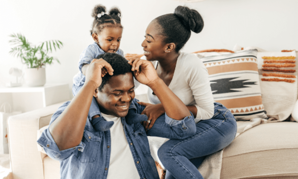 Happy young family spending time together at home — mom, dad, and toddler smiling and playing in a living room. Perfect image for family protection and life insurance themes in the Lehigh Valley.