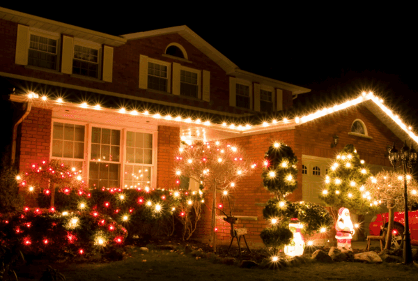 Festively decorated brick house in Pennsylvania illuminated at night with Christmas lights outlining the roof, bushes, and trees, featuring glowing Santa and snowman yard decorations.