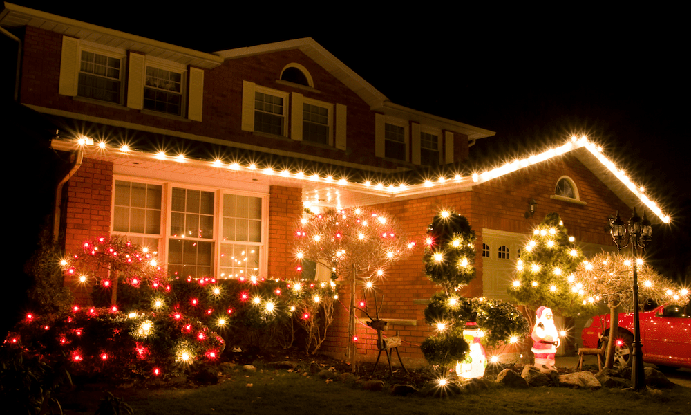 Festively decorated brick house in Pennsylvania illuminated at night with Christmas lights outlining the roof, bushes, and trees, featuring glowing Santa and snowman yard decorations.
