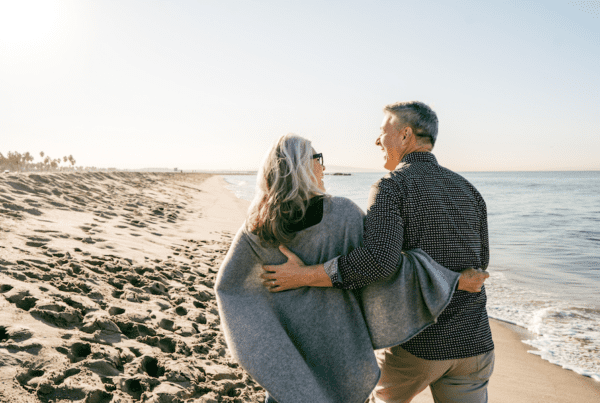 A happy couple enjoying a Valentine’s Day walk on the beach, highlighting the importance of life insurance as a lasting act of love and financial protection.