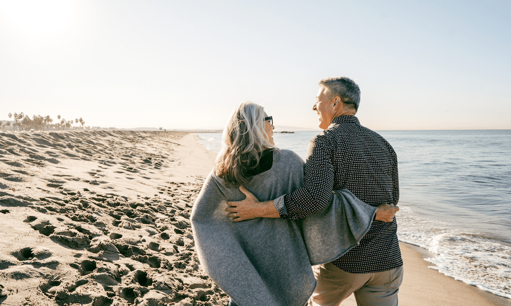 A happy couple enjoying a Valentine’s Day walk on the beach, highlighting the importance of life insurance as a lasting act of love and financial protection.