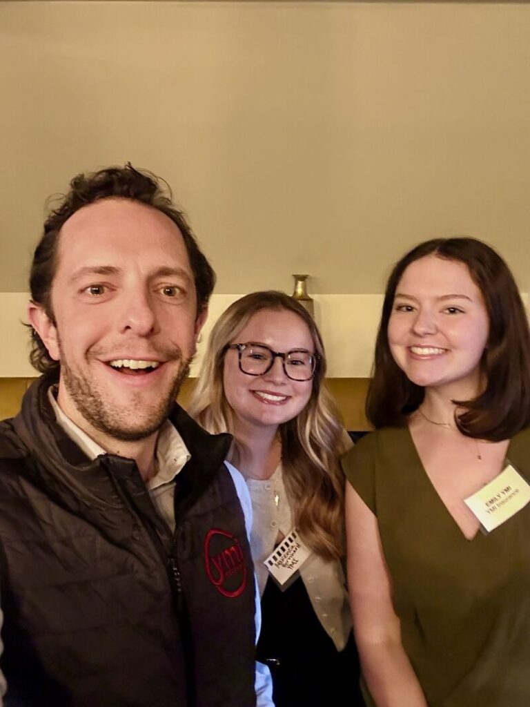 Three attendees at a business networking event in Allentown pose for a smiling selfie indoors, wearing name tags, with a warm, casual atmosphere in the background