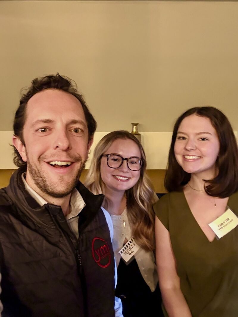 Three attendees at a business networking event in Allentown pose for a smiling selfie indoors, wearing name tags, with a warm, casual atmosphere in the background