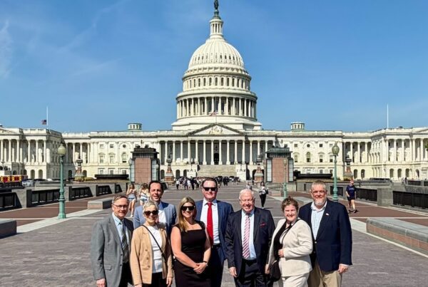 Jimi Honochick standing with a group in front of the U.S. Capitol building on a clear day, posing on the walkway with the Capitol dome centered behind them.