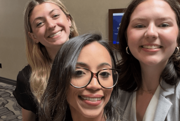 Modesty, Emily, and Peyton smiling for a selfie at a professional event, wearing name badges.