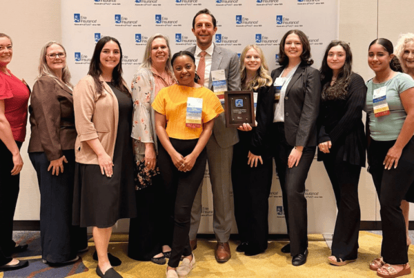 Group photo of attendees at an Erie Insurance event, standing in front of a branded backdrop with an award recipient holding a plaque